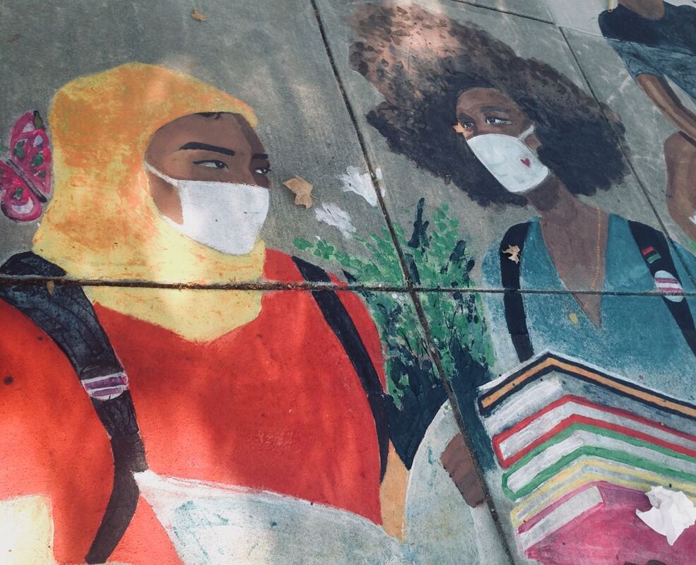 Photo of mural on concrete, showing young woman in hajib talking to woman with afro, carrying books